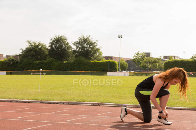 Jeune femme athlétique attacher lacets de chaussures sur une piste de course — Photo de stock