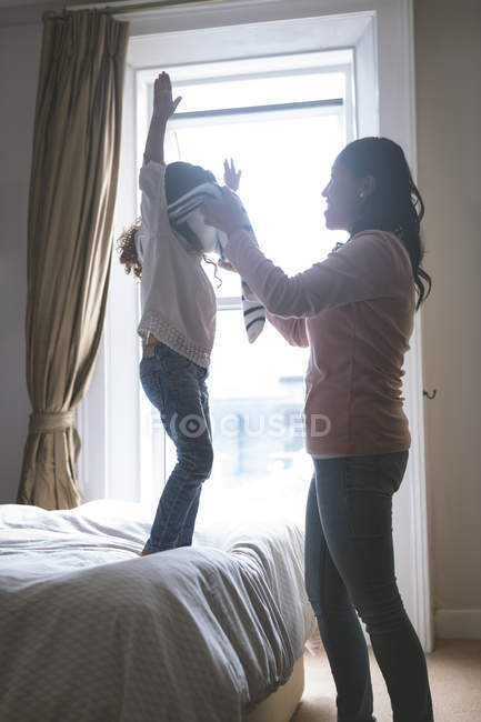 Mother helping her daughter in wearing cloth at home — Stock Photo