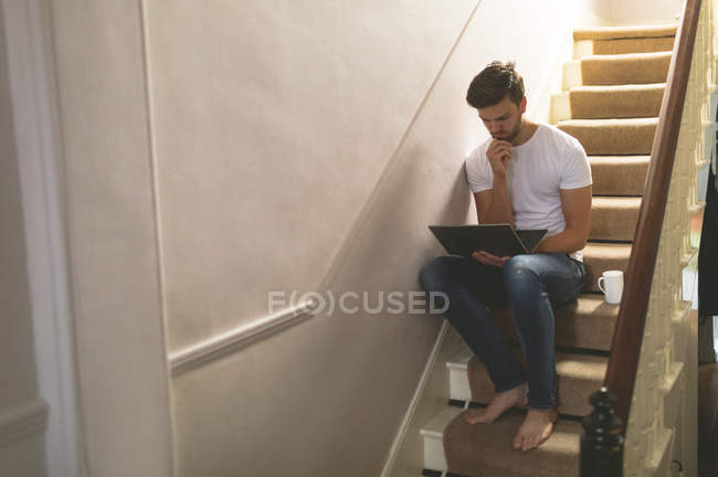 Jeune homme utilisant un ordinateur portable sur l'escalier à la maison — Photo de stock