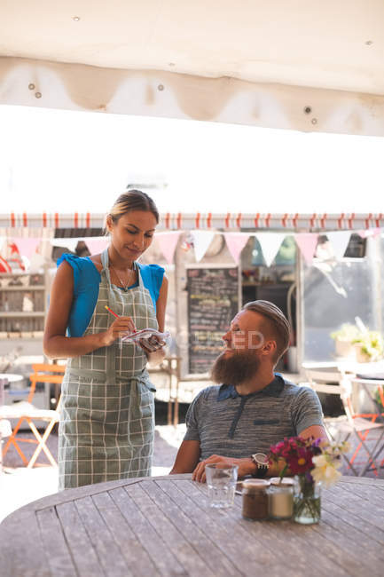 Жіноча офіціантка робить замовлення у відкритому кафе на сонячний день — стокове фото