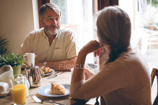 Casal sênior interagindo uns com os outros enquanto toma café da manhã em casa — Fotografia de Stock