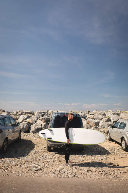 Серфер держит доску для серфинга возле пляжа в солнечный день — стоковое фото