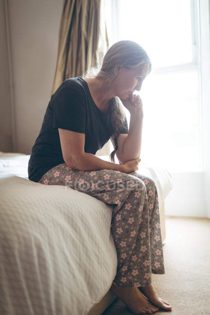 Femme âgée inquiète assise sur le lit dans la chambre à coucher à la maison — Photo de stock