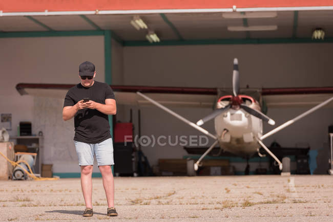 Mécanicien utilisant un téléphone portable au hangar aérospatial — Photo de stock