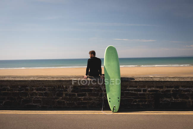 Вид ззаду серфера з дошкою для серфінгу, що сидить на навколишній стіні — стокове фото