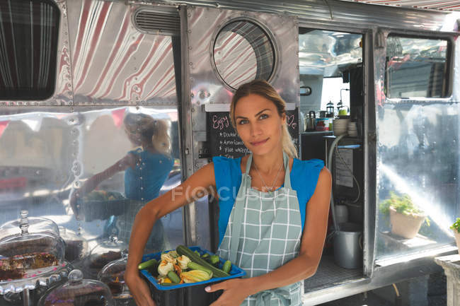 Female waitress holding vegetables in basket near food truck — Stock Photo
