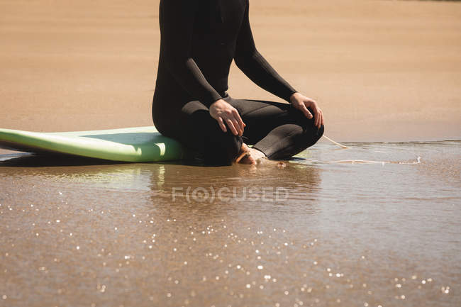 Baixa seção de surfista sentado na prancha de surf na praia — Fotografia de Stock