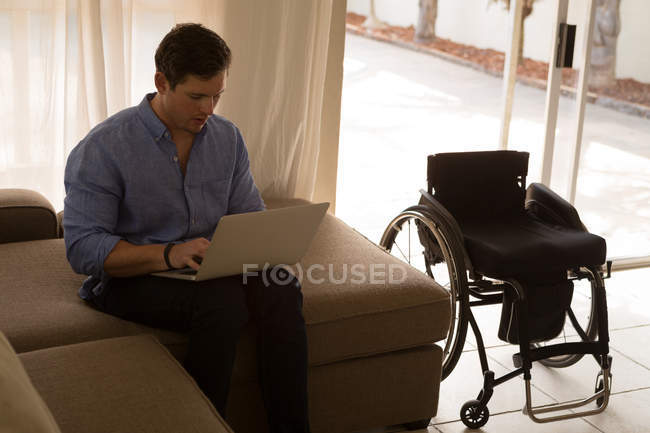 Людина з обмеженими можливостями використовує ноутбук у вітальні вдома — стокове фото