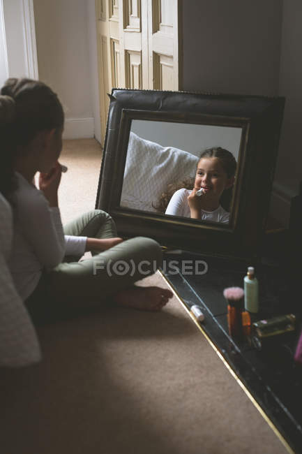 Chica aplicando lápiz labial delante del espejo en casa - foto de stock