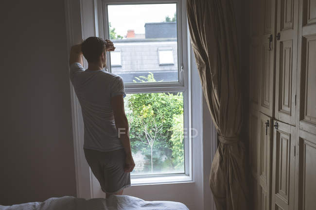 Задній вид людина дивиться через вікно на дому — стокове фото