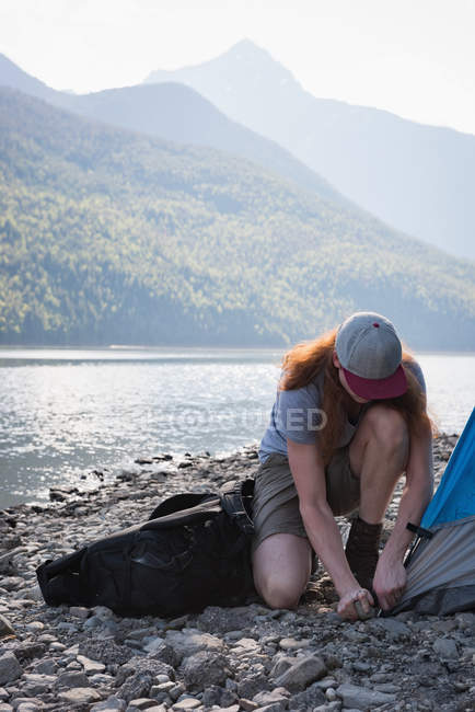 Человек расставляет палатку у реки в горах — стоковое фото