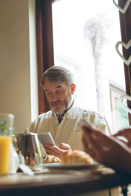 Старший чоловік використовує цифровий планшет під час сніданку вдома — стокове фото