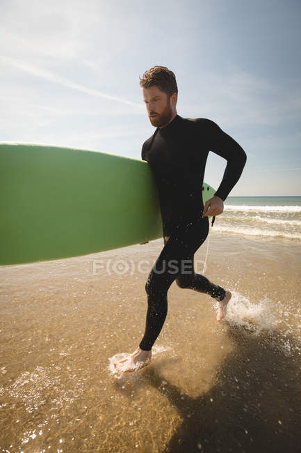 Surfista com prancha correndo na praia em um dia ensolarado — Fotografia de Stock