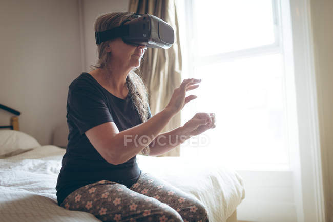 Старша жінка використовує гарнітуру віртуальної реальності в спальні вдома — стокове фото