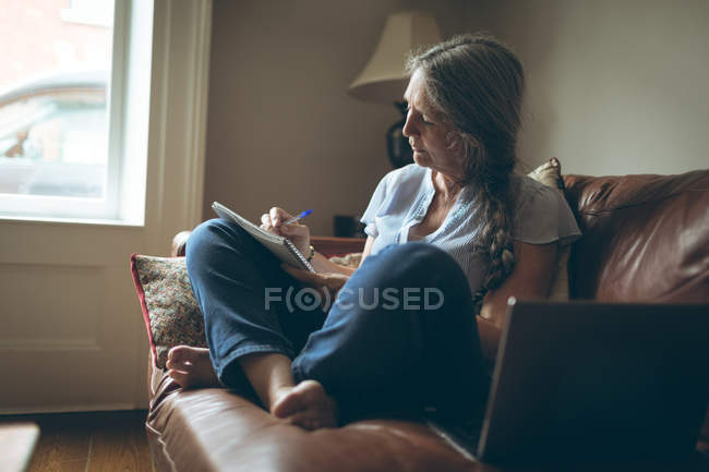 Senior woman writing on a notepad in living room at home — Stock Photo