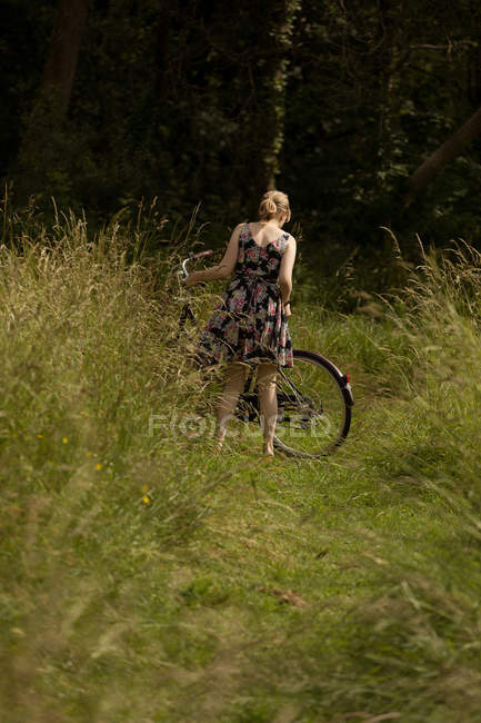 Vista posteriore della donna in piedi con bicicletta nel campo — Foto stock