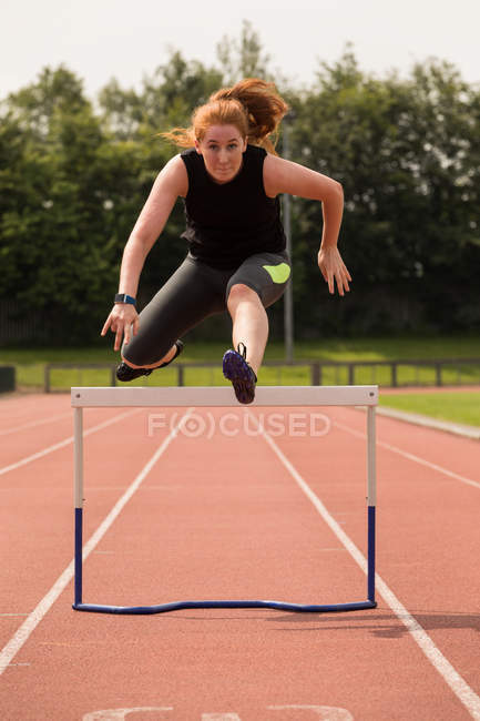 Young female athletic running over hurdle on sports track — Stock Photo