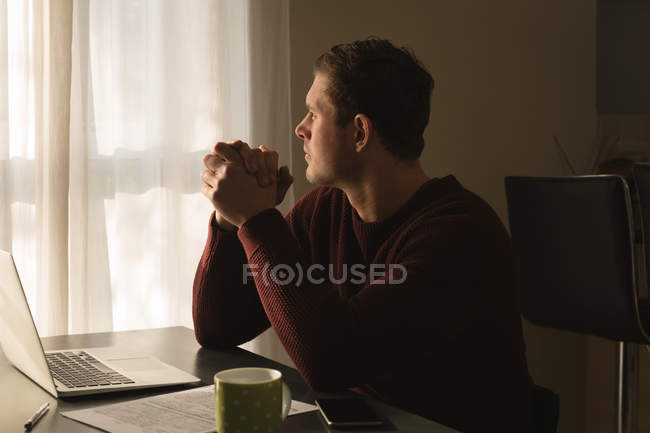 Задумчивый человек смотрит в окно на дом — стоковое фото