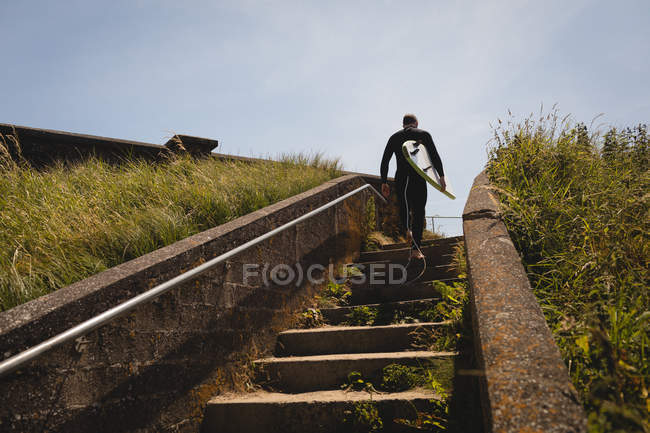 Low angle view of surfer with surfboard walking on staircase — Stock Photo