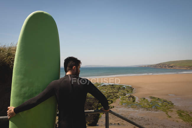 Rear view of surfer with surfboard standing on staircase — Stock Photo