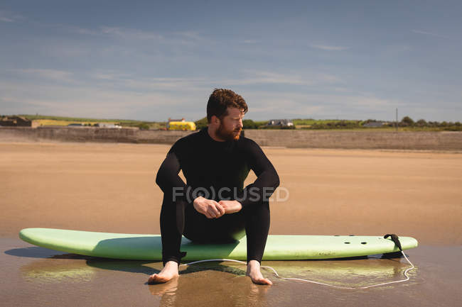 Серфер, сидящий на доске для серфинга на пляже в солнечный день — стоковое фото