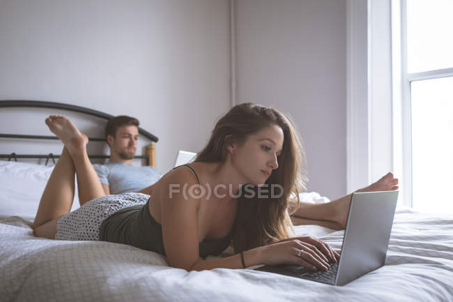 Coppia utilizzando laptop e tablet digitale in camera da letto a casa — Foto stock
