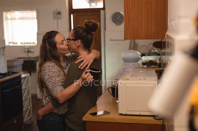 Лесбиянки целуются дома на кухне — стоковое фото