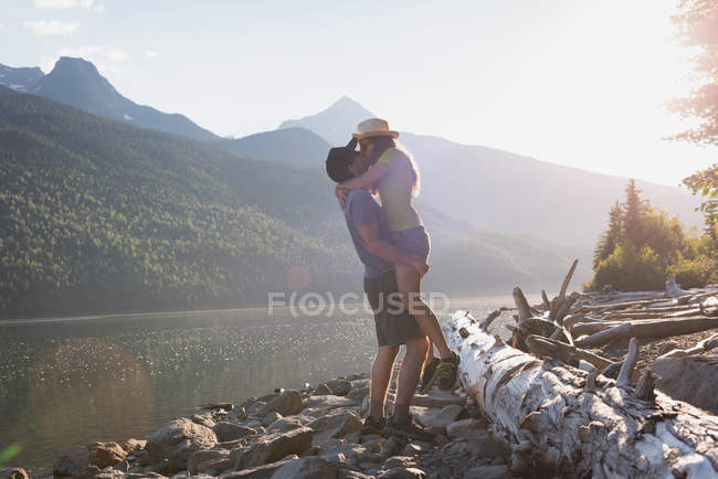 Pareja besándose cerca de la orilla del río en las montañas - foto de stock