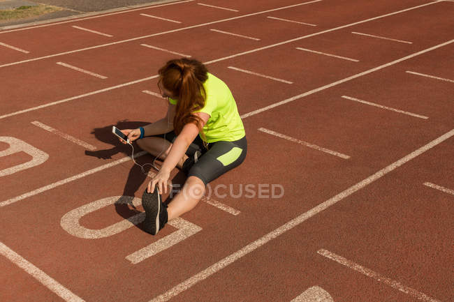 Giovane atletica femminile utilizzando il telefono cellulare durante l'esercizio sulla pista di corsa — Foto stock