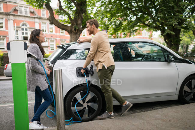 Paar interagiert beim Laden von Elektroautos an Ladestation miteinander — Stockfoto