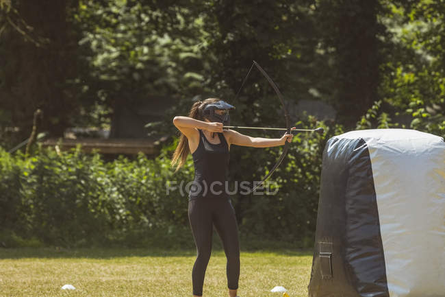 Mulher praticando tiro com arco no campo de treinamento em um dia ensolarado — Fotografia de Stock