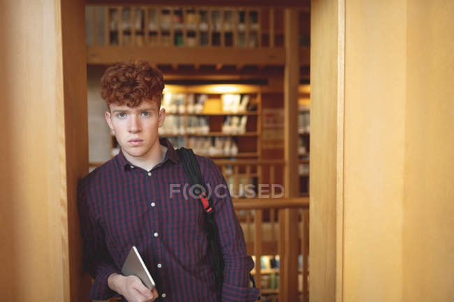 College student with digital tablet looking at camera in library — Stock Photo