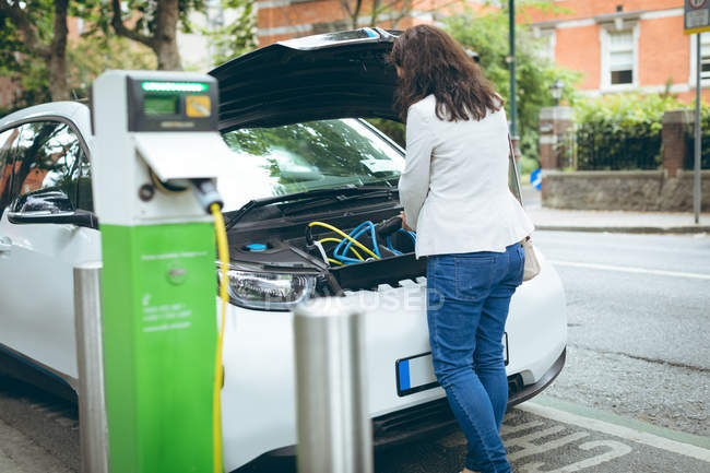 Вид сзади на деловую женщину, заряжающую электромобиль на зарядной станции — стоковое фото