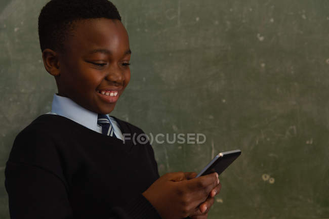 Écolier utilisant un téléphone portable près du tableau dans la salle de classe — Photo de stock