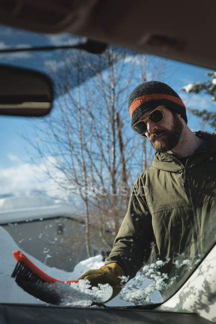 Man cleaning snow from car windshield during winter — Stock Photo