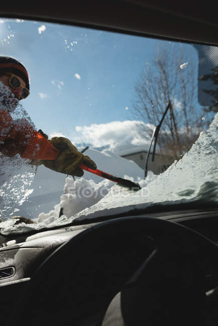 Человек очищает снег от лобового стекла автомобиля зимой — стоковое фото