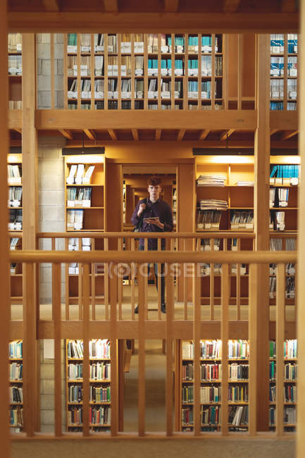 Studentin mit digitalem Tablet blickt in Bibliothek auf Kamera — Stockfoto