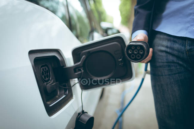 Gros plan de l'homme d'affaires rechargeant une voiture électrique à la station de recharge — Photo de stock