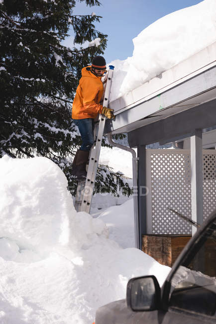 Man climbing on a ladder to clean snow from roof top of his shop during winter — Stock Photo