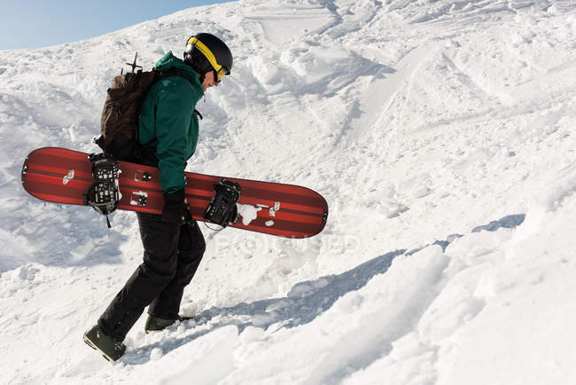 Esquiador caminando con tabla de esquí en una montaña nevada durante el invierno - foto de stock
