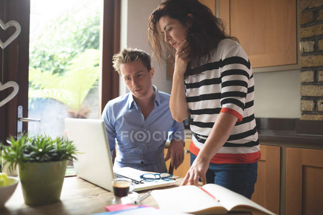 Attentive couple discussing over laptop in kitchen at home — Stock Photo