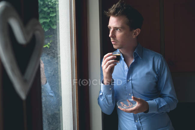 Thoughtful man looking through window while having coffee at home — Stock Photo