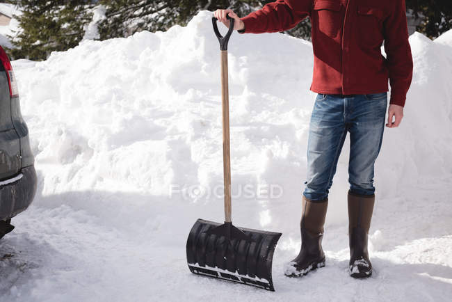Чоловік стоїть зі сніговим лопатою на засніженому регіоні взимку — стокове фото