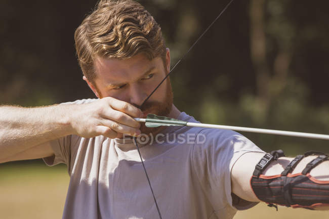 Mann übt sich an einem sonnigen Tag im Bogenschießen im Bootcamp — Stockfoto