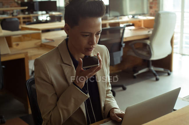 Executive using laptop while talking on mobile phone in office — Stock Photo