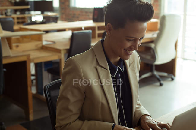 Ejecutivo sonriente usando el ordenador portátil en el escritorio en la oficina - foto de stock