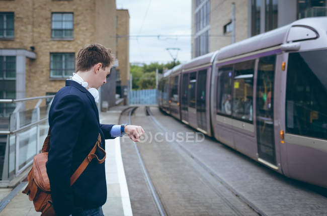 Uomo d'affari che controlla l'ora nel suo smartwatch alla stazione ferroviaria — Foto stock