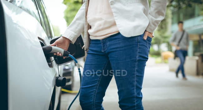 Средняя секция деловой женщины, заряжающей электромобиль на зарядной станции — стоковое фото