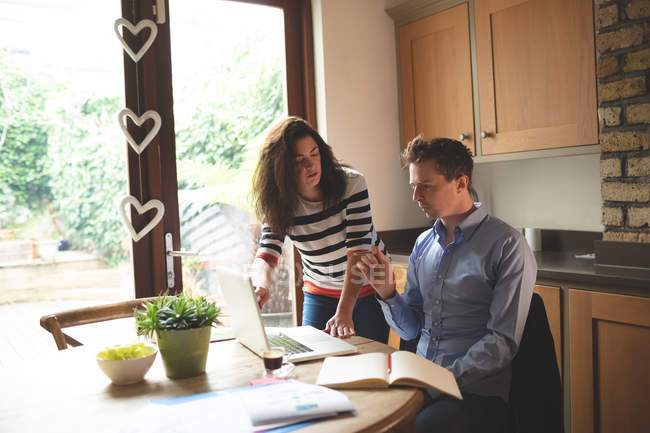 Casal discutindo sobre laptop na cozinha em casa — Fotografia de Stock