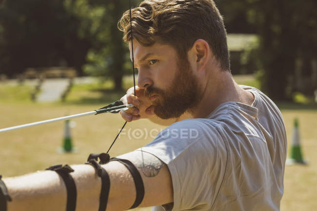 Mann übt sich an einem sonnigen Tag im Bogenschießen im Bootcamp — Stockfoto